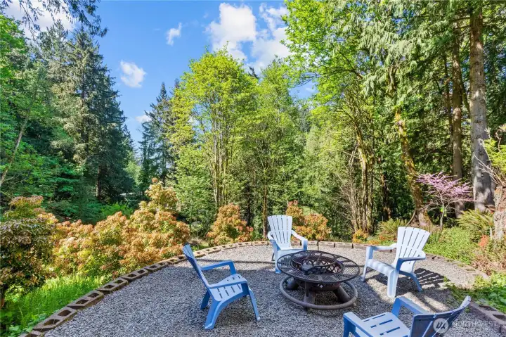 Outdoor patio area with fire pit seating surrounded by mature landscaping and peaceful forest views.