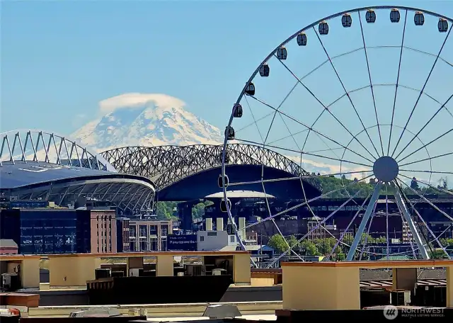 Majestic Mount Rainier, crowned with its ethereal cap cloud, stands as a breathtaking backdrop to the vibrant city & 20 acre Waterfront Park. Nearby T-Mobile Park and Lumen Field pulse with the energy of sports fans, while The Seattle Great Wheel stands out along the waterfront.