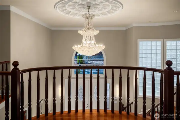Dramatic chandelier and custom ceiling detail above the sweeping staircase landing.