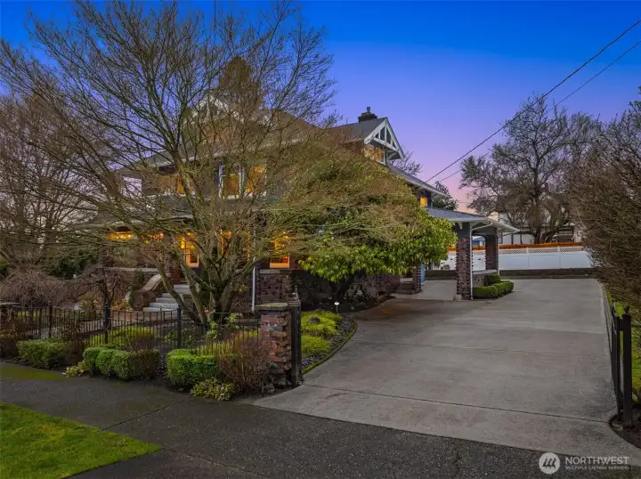 As dusk settles, the gated entry sets a quiet, distinguished tone—framing the home in soft light and signaling arrival to a place of substance and privacy. Brick pillars, mature landscaping, and a sweeping drive create a sense of ceremony, while the glow from within hints at the warmth and history waiting beyond the gate. This is not simply an entrance, but a gracious welcome home.