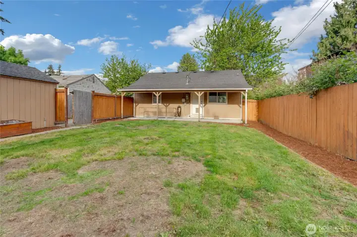 Fully fenced yard with a raised bed on the left. The stairs that go to the basement are on the left under the patio cover.