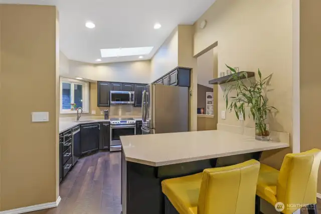The updated kitchen features quartz counters, painted cabinetry, and stainless steel appliances. A vaulted ceiling with a skylight ensures this space remains light-filled throughout the day.