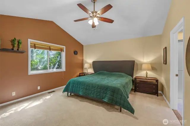 The private primary suite boasts vaulted ceilings, soft new carpet, and garden views from the large window. Its generous proportions offer a restful retreat with easy access to the en-suite bath.