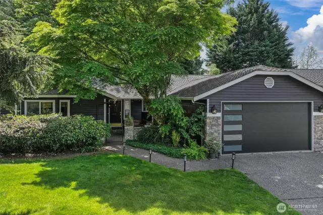 A closer view highlights the lush greenery and thoughtfully designed entry path, creating a warm, private approach to the front door. The wide driveway and well-maintained lawn enhance the home’s inviting presence.