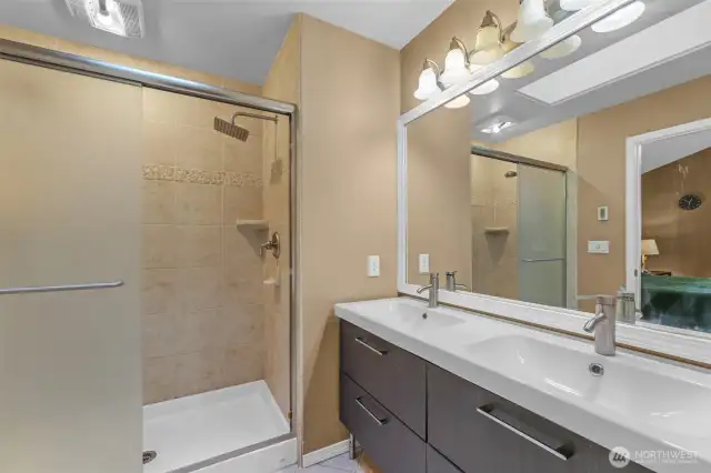 The private three-quarter en-suite bathroom features a dual-sink vanity with modern fixtures and an oversized mirror. The tiled walk-in shower includes an accent border and built-in shelf, offering both function and style.