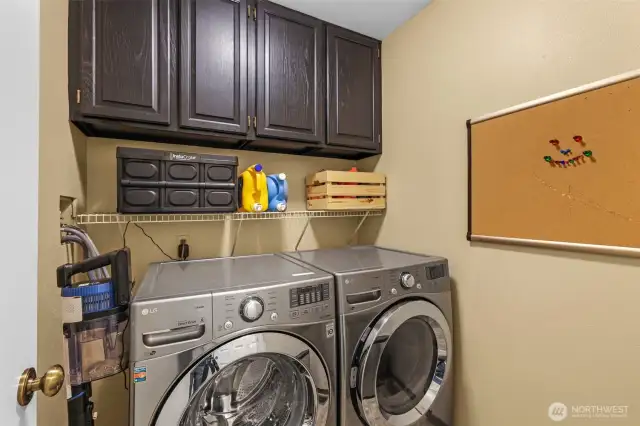 The well-organized laundry room is outfitted with full-size washer and dryer, overhead cabinetry for supplies, and a practical wire shelf. Everything is within reach for streamlined routines.