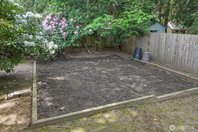 The rear garden includes a framed planting area that’s perfect for raised beds, seasonal flowers, or a future play zone. Blooming rhododendrons add a burst of Pacific Northwest color.