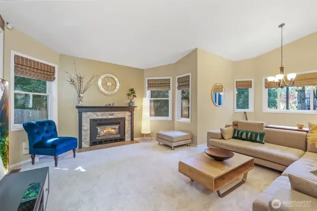 The spacious living room features high ceilings and abundant windows that bathe the space in natural light. The cozy gas fireplace with a stone surround offers year-round ambiance and warmth, anchoring the room beautifully.