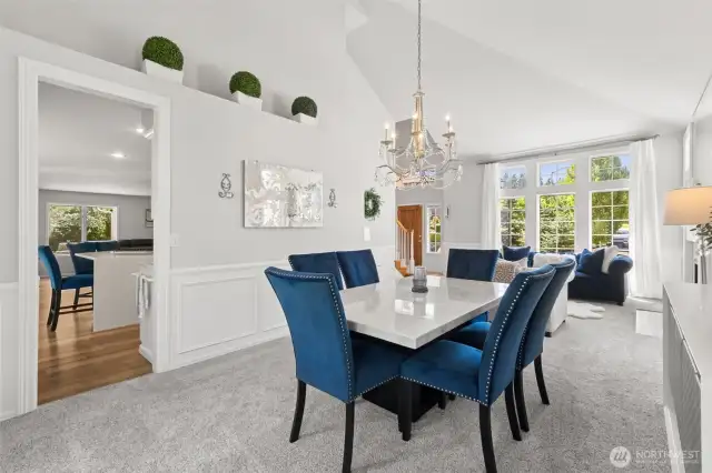 Formal Dining & Living Room Combo - soaring vaulted ceilings and oversized windows flood this elegant formal dining and living area with natural light. Features a sparkling chandelier, wainscoting details, and plush carpet. A seamless layout perfect for entertaining or relaxing in style.