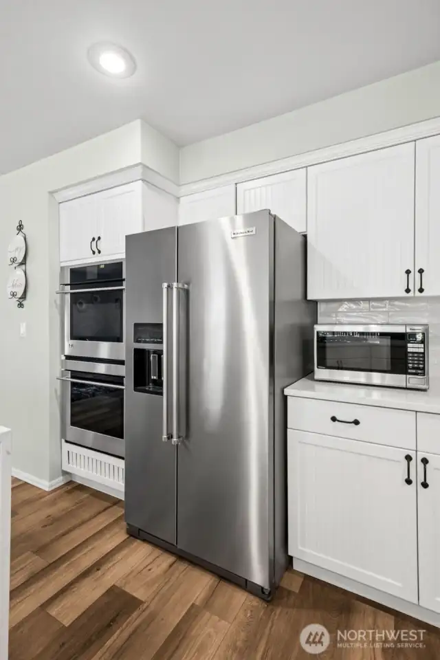 High-end Monogram double oven and KitchenAid stainless steel appliances complement the clean white cabinetry. Sleek finishes and abundant storage combine style and functionality in this gourmet kitchen.