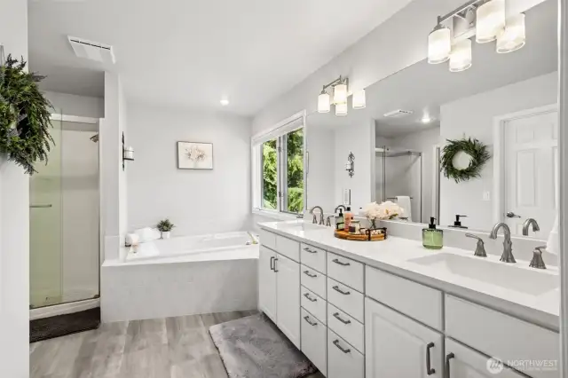 Bright and tranquil ensuite showcasing dual vanities, a large jetted soaking tub, and separate shower. Natural light pours in through the window, offering serene views and a luxurious atmosphere.