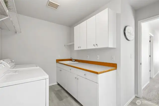 Functional Laundry Room with Utility Sink.   Spacious laundry room featuring full-size washer and dryer, built-in utility sink, and abundant cabinetry for storage. Durable flooring and countertop space make chores convenient and efficient.