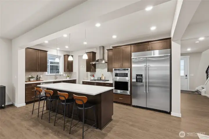 Gourmet kitchen with large center island, quartz counters, loads of cabinets, built-in 48" fridge and in-wall oven & microwave next to your large family room. Materials, colors, and finishes will vary. See site agent for details