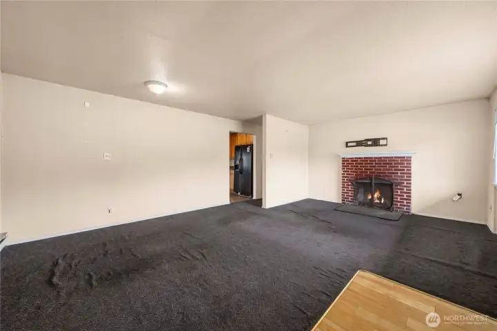 Living room from the corner with the entry at the front right and kitchen in the background. Fire is photoshopped into the fireplace!