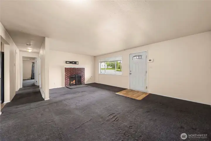 Living room as seen from the far corner. Front entry on the right and hallway on the left. Far left is the kitchen. Fire has been photoshopped into the fireplace.
