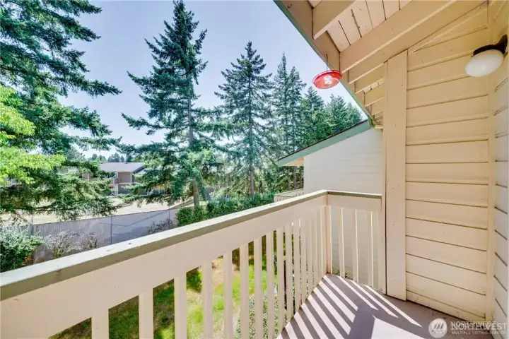 Private covered balcony overlooking mature trees and landscaped grounds, offering a peaceful outdoor living space.