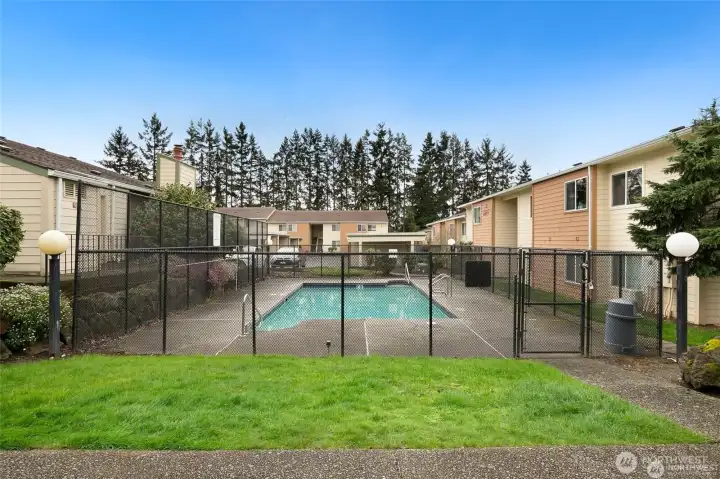 Community swimming pool surrounded by landscaped grounds and residential buildings, offering convenient outdoor recreation and relaxation for condominium residents.
