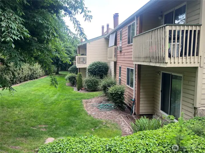 Rear exterior of condominium building with private balconies, landscaped green space, mature trees, and well-maintained community grounds.