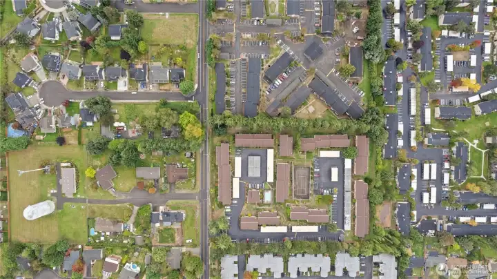 Aerial view of condominium community featuring residential buildings, swimming pool, sport court, landscaped grounds, and resident parking.
