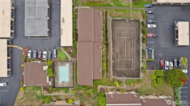 Aerial view of condominium community amenities including swimming pool, sport court, landscaped grounds, and resident parking areas.