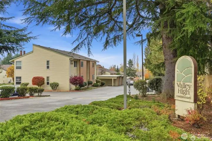 Valley High Condominium community entrance sign surrounded by mature trees, landscaped grounds, and residential buildings.