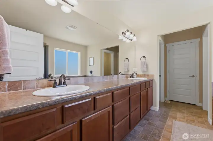 Primary en suite, with two sinks, linen closet at the back, main bedroom closet to the left, and enclosed toilet area to the right.