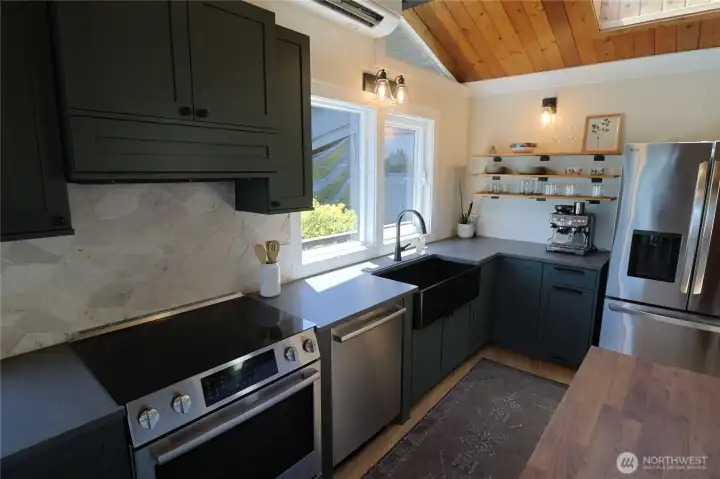 The updated main floor kitchen is a dream with skylights, dark cabinetry, a farmhouse sink, stone backsplash, and stainless steel appliances All appliances stay.