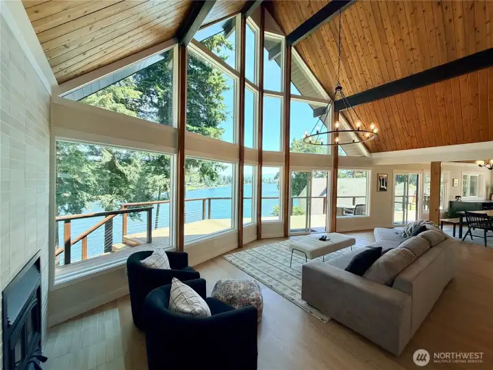 The great room delivers everything at once: soaring vaulted A-frame ceilings with gorgeous wood beams, a cozy updated wood fireplace, gleaming luxury floors, and a panoramic wall of windows overlooking the lake and deck. This is the room you will never want to leave.