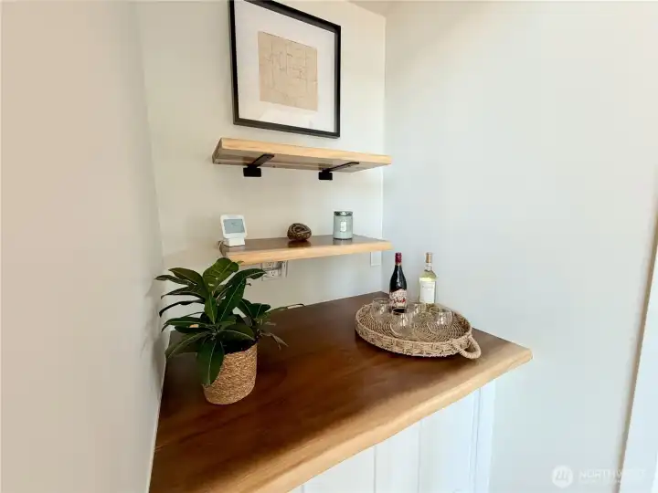 A thoughtful built-in wine and bar nook with a wood countertop, storage for firewood, and floating shelves adds a charming finishing touch to the main living area. Pour a glass, watch the lake, and settle in.