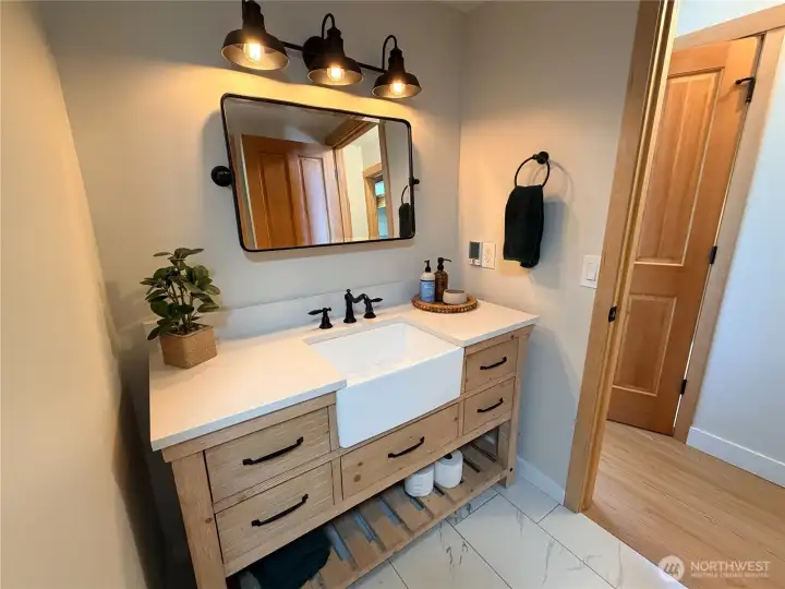 The updated main level bathroom features a farmhouse sink vanity, quartz countertop, black hardware, and designer lighting. Every bathroom in this home has been thoughtfully renovated.