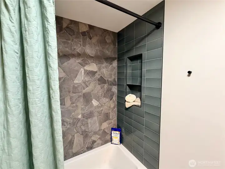 The shower in the main level bathroom is also updated and equally stunning with green tile, stone, black accents, and a built-in for storage.
