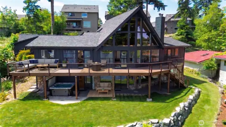 The back of this home is nothing short of showstopping, with a massive composite deck, covered patio, hot tub, and lush green yard that make outdoor living here feel like a private resort. Some outdoor furniture is virtually staged.