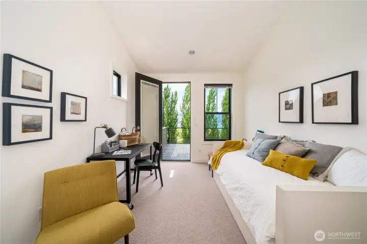 View of upper level King ensuite bedroom 2 with vaulted ceilings, sitting area with bonus twin daybed and trundle for two additional guests, a work station, and glass doors leading to the outdoor lake view deck.