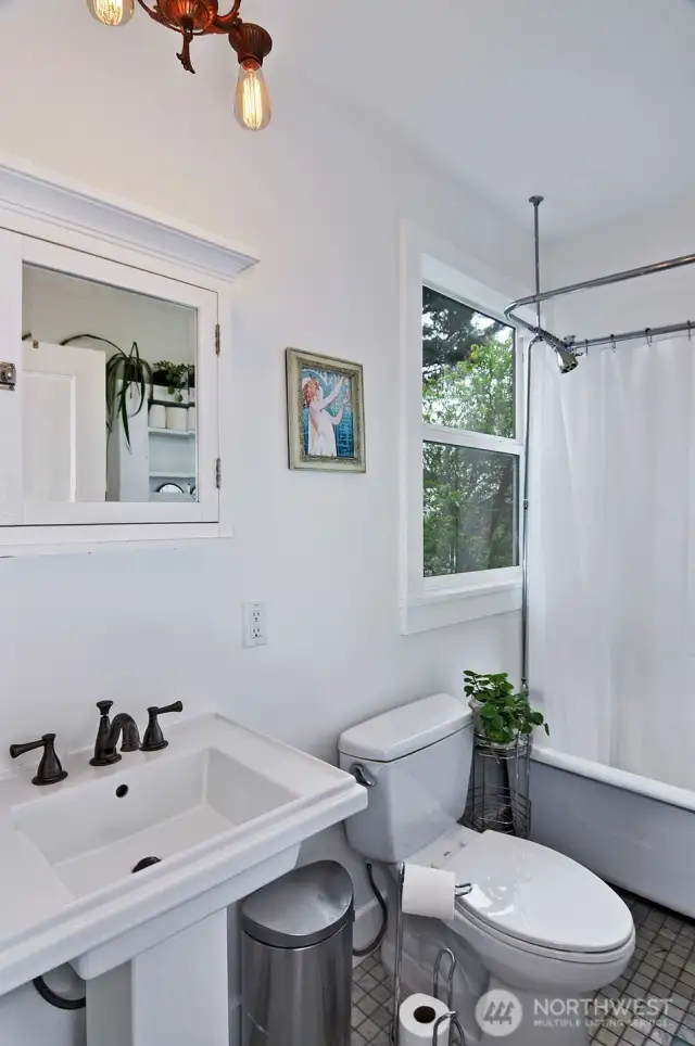 The full size bath on the main floor- Just around the corner from the kitchen. Tiled floors, porcelain vanity, clawfoot tub with a large window looking out the back yard, vintage lighting.