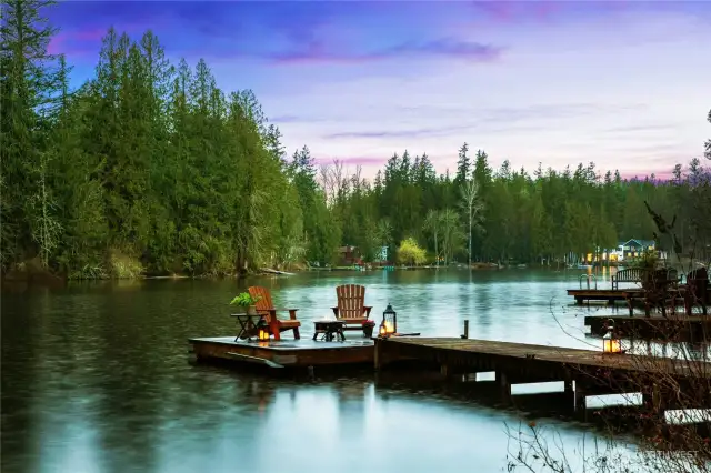 Stunning Sammamish lakefront living aglow at dusk. Evenings by the lake - unwind on your private dock as the sun sets over calm waters and a tranquil shoreline. Tour the lake and visit with friends and neighbors on your floating barge on Beaver Lake. Serene Sammamish waterfront retreat awaits with direct lake access.
