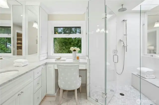 Natural light pours into this serene primary bath with marble surfaces, vanity seating, and tranquil views of the lake just outside.