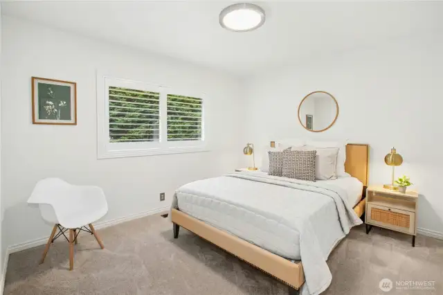 Peaceful secondary bedroom with plush carpet, closet system, and a large window framing lush green views.