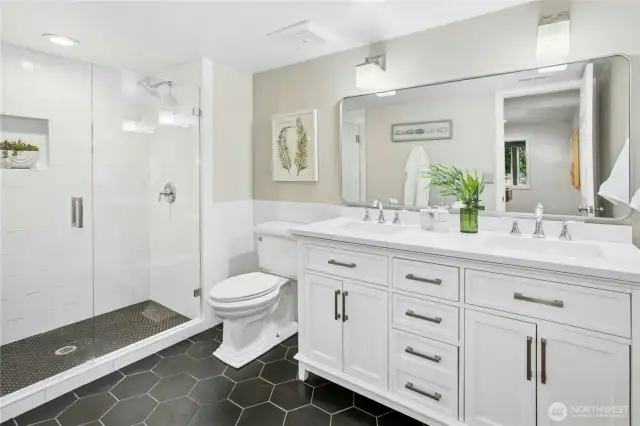 Stylishly updated 3/4 bathroom with dual vanity, designer tile, and frameless walk-in shower on the lower level, adjacent to the guest bedroom.