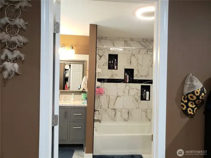 Primary Master Bath Room Showing New Vanity with Granite Counter Top, Tub Tile Surround, Sink, Faucet, Paint, Mirror, LED Lighting and Tile Flooring.