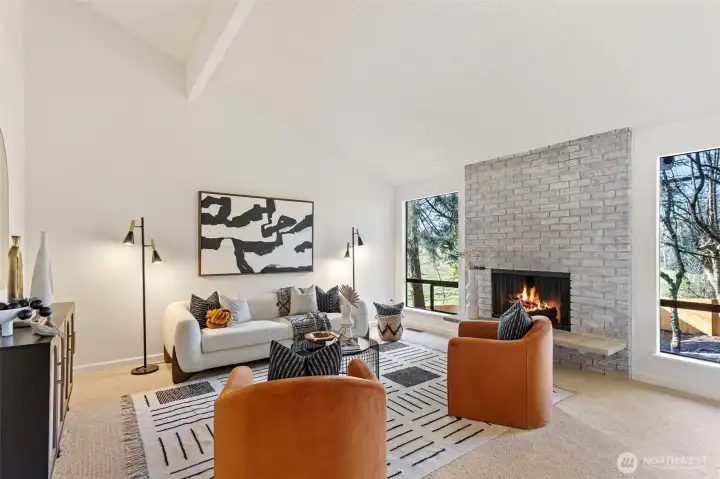 The living room boasts vaulted ceilings with an exposed beam, a cozy wood burning fireplace and large windows overlooking the private grounds.