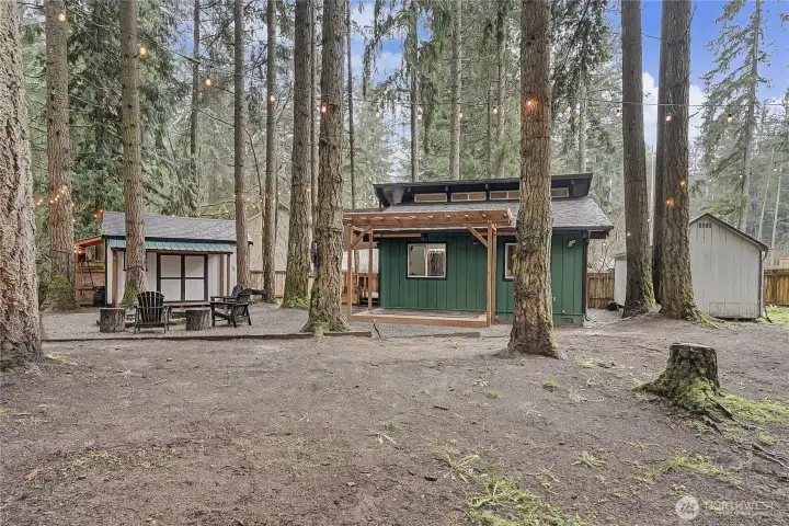 View of the cabin and additional shed/guest bedroom from back of yard, additional covered deck on the back. Love  the tall trees!