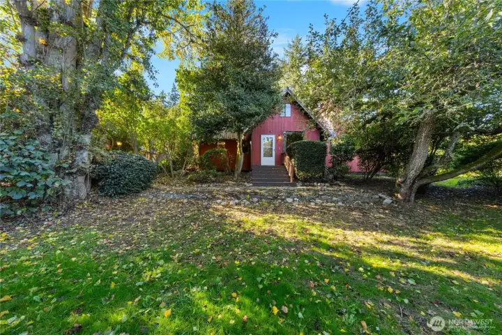 Charming red cottage nestled among mature trees, offering a peaceful, private setting surrounded by natural beauty.