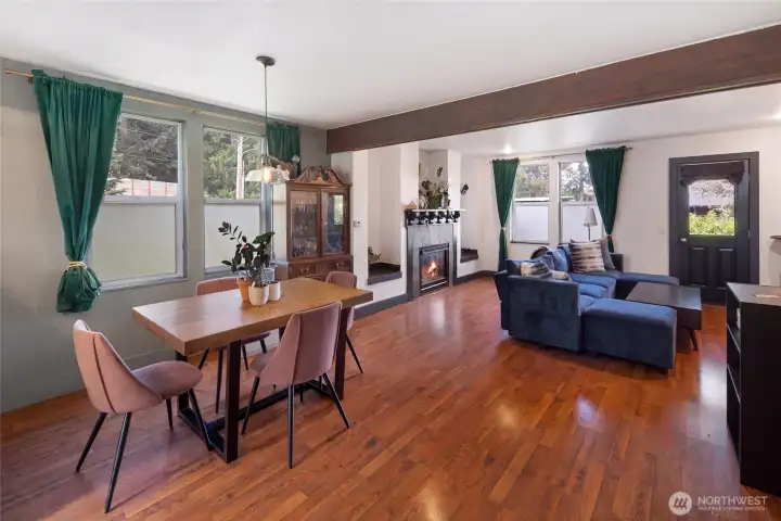 The open-concept living and dining area exudes warmth with gleaming laminate floors, a decorative beam, and a cozy propane fireplace anchoring the space. Rich jewel-toned accents and abundant natural light create an inviting, move-in-ready atmosphere perfect for everyday living and entertaining.