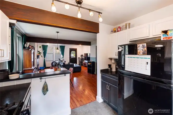 The kitchen opens effortlessly into the dining and living areas through a wide, beam-framed passage, creating a connected, social layout that feels spacious and inviting. Durable, easy-care finishes throughout the kitchen and into the adjoining living space make this open-concept floor plan as practical as it is charming for everyday island living.