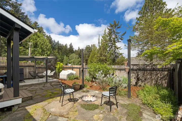 A lovingly designed backyard garden retreat features a stone firepit seating area, pergola with string lights, lush perennial plantings, and a flagstone patio — the kind of outdoor living space that makes island evenings unforgettable. This private, fully fenced sanctuary feels like a secret garden tucked in the heart of Friday Harbor.
