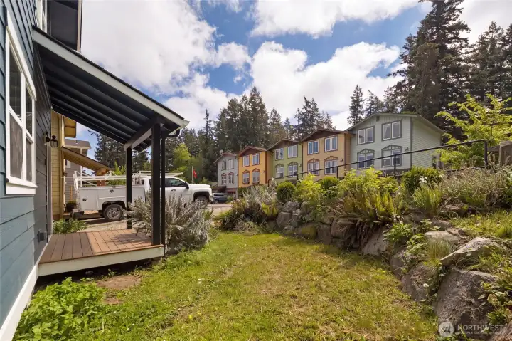 A covered entry deck and gently sloped front yard offer additional outdoor living space, with a vibrant, walkable neighborhood backdrop of colorful homes and towering evergreens — quintessential Friday Harbor island character.