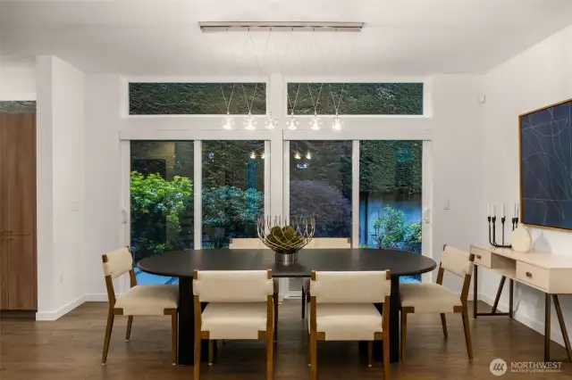 Wall of windows in the dining room space that is graced by mature landscaping.