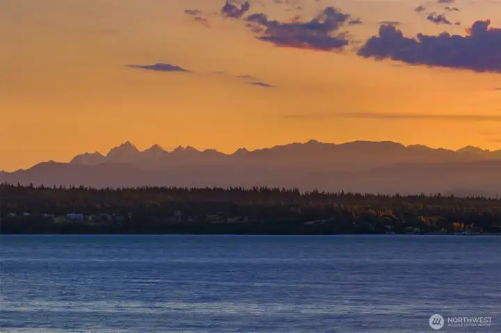 The Olympic Mountains provide a breathtaking backdrop, rising above the crystal-blue waters below to create a view that is nothing short of spectacular.