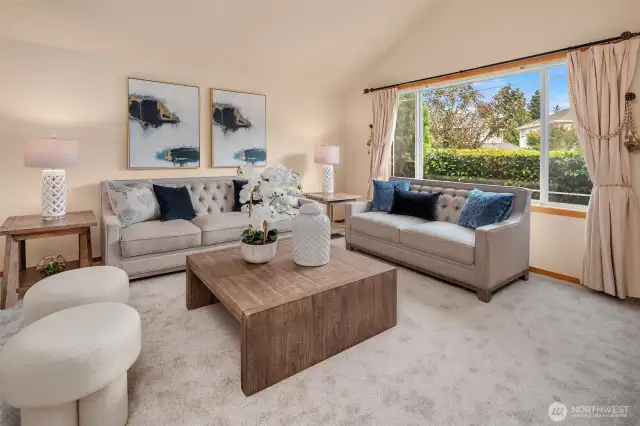 The bright living room boasts oversized windows framing lush greenery