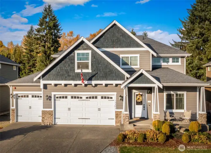 A beautiful two-story home with strong curb appeal, featuring a three-car garage, stone accents, and a welcoming covered front porch. The exterior is finished in timeless neutral tones with crisp white trim, set against a backdrop of mature trees for added privacy. The well-kept front landscaping frames the entry and highlights the home’s classic Northwest style.